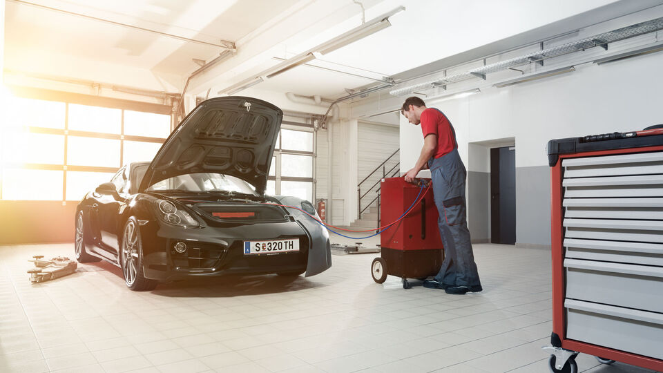Eine Servicetechnikerin poliert die Motorhaube eines roten Porsche