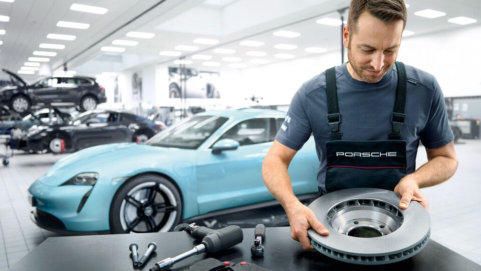 Ein Mechaniker mit einem Ersatzteil für ein Porsche Auto