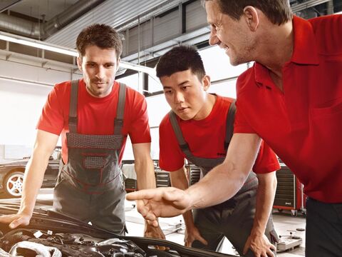3 Techniker blicken in den Motorraum eines Porsches