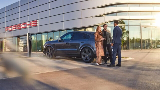 3 Personen unterhalten sich vor einem Porsche Zentrum