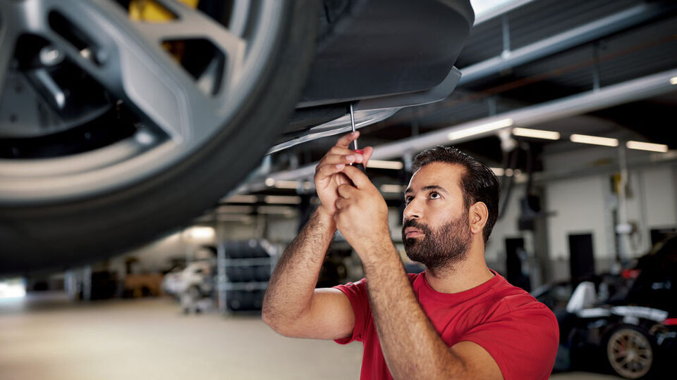 Ein Techniker schraubt an der Unterseite eines Porsches