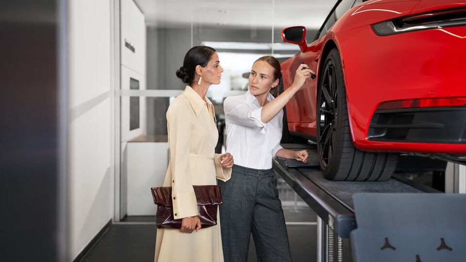 Zwei Frauen stehen neben mit einer Hebebühne mit einem roten Porsche