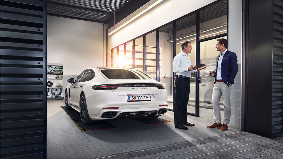 3 Personen unterhalten sich vor einem Porsche Zentrum