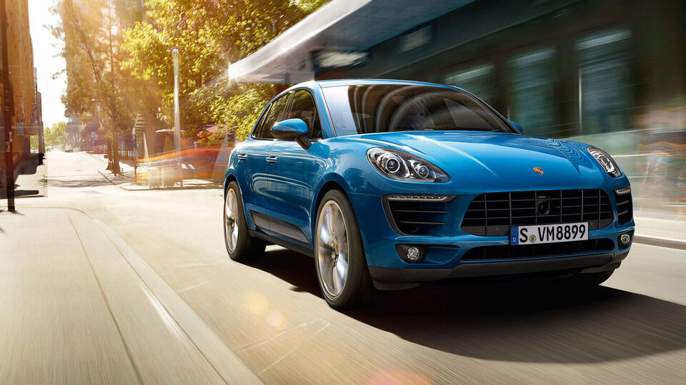 Blauer Porsche Cayenne fährt eine Straße entlang.