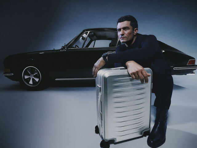 Orlando Bloom vor einem 911 Porsche mit dem neuen Aluminium Trolley