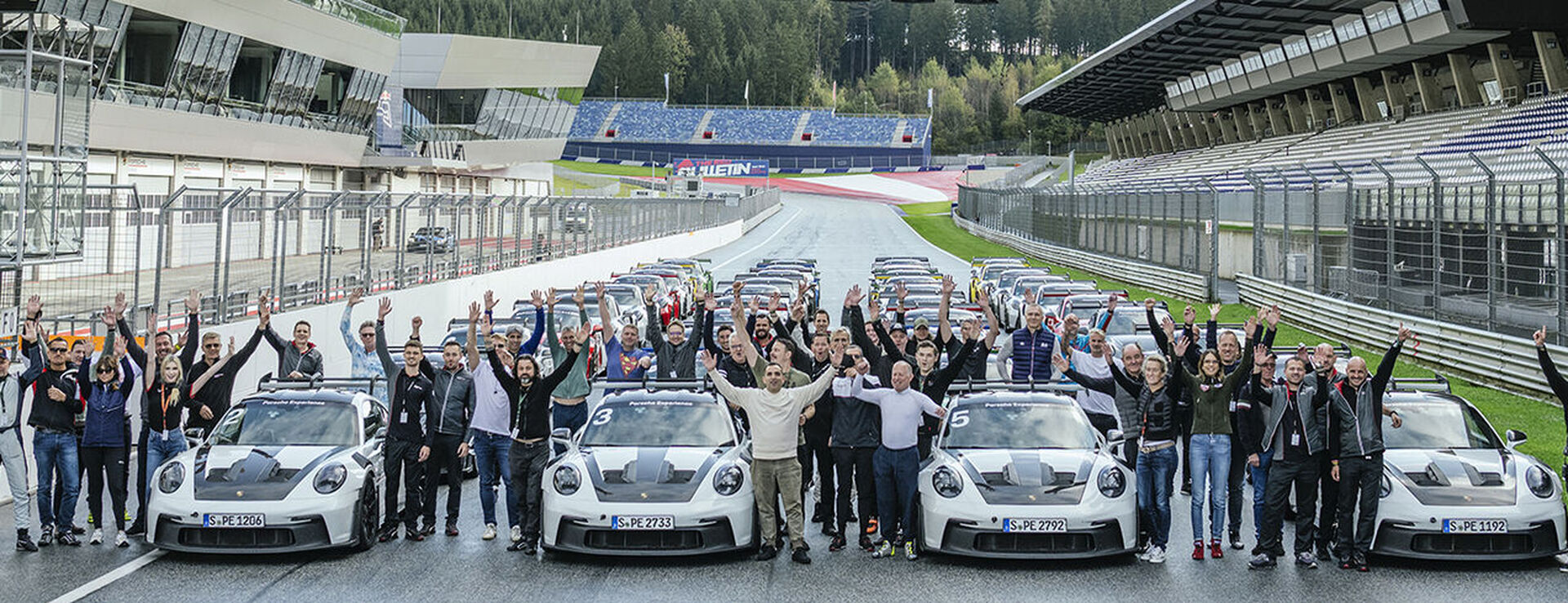 Ein Mann lehnt sich an die Motorhaube eines weißen Porsche Cayennes, während eine Frau vorbei geht.